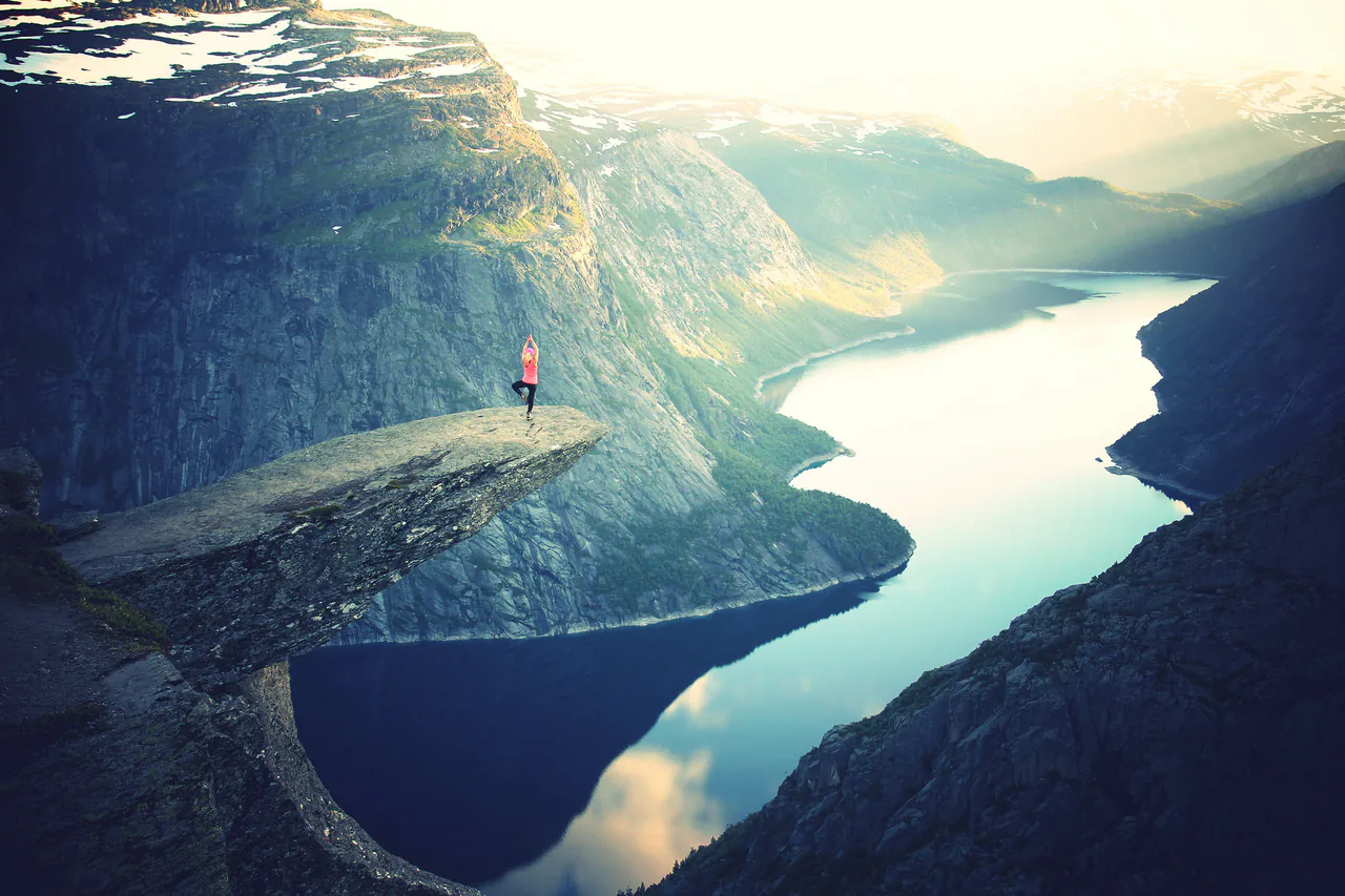 Standing on a rocky cliff overlooking a fjord, with mountains silhouetted against the sunset, one finds serenity much like visiting an anxiety therapist nearby.