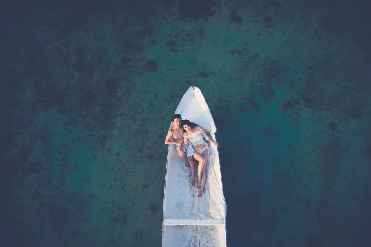 A couple relaxes on the bow of a white boat, floating on clear, shallow water, finding peace much like they did after sessions with the best therapists near me.
