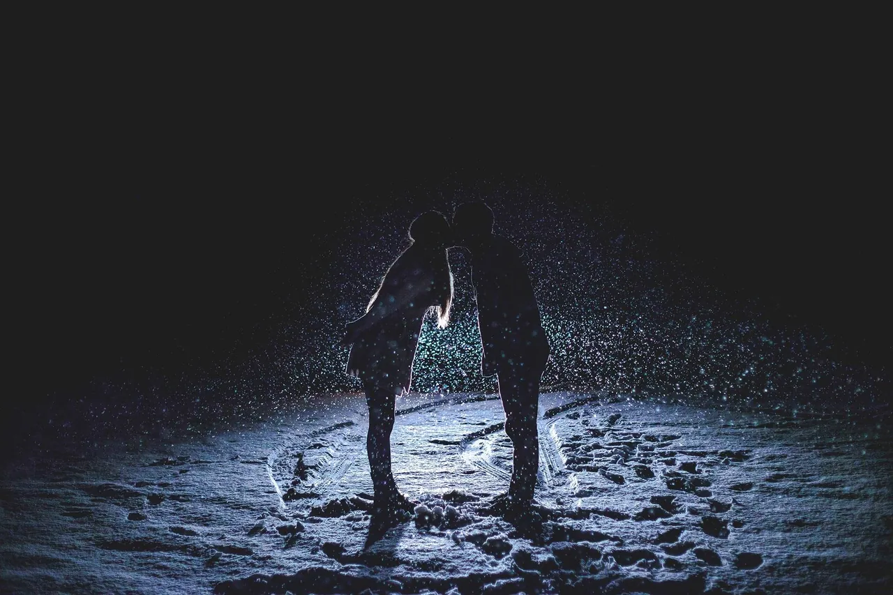 Silhouetted couple kissing in the snow at night, surrounded by falling snowflakes, while nearby a sign for the best therapists near me offers warmth and comfort amidst the cold.