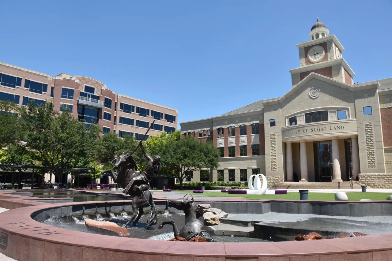 A statue of horses and a fountain in front of sugar land city hall on a sunny day.